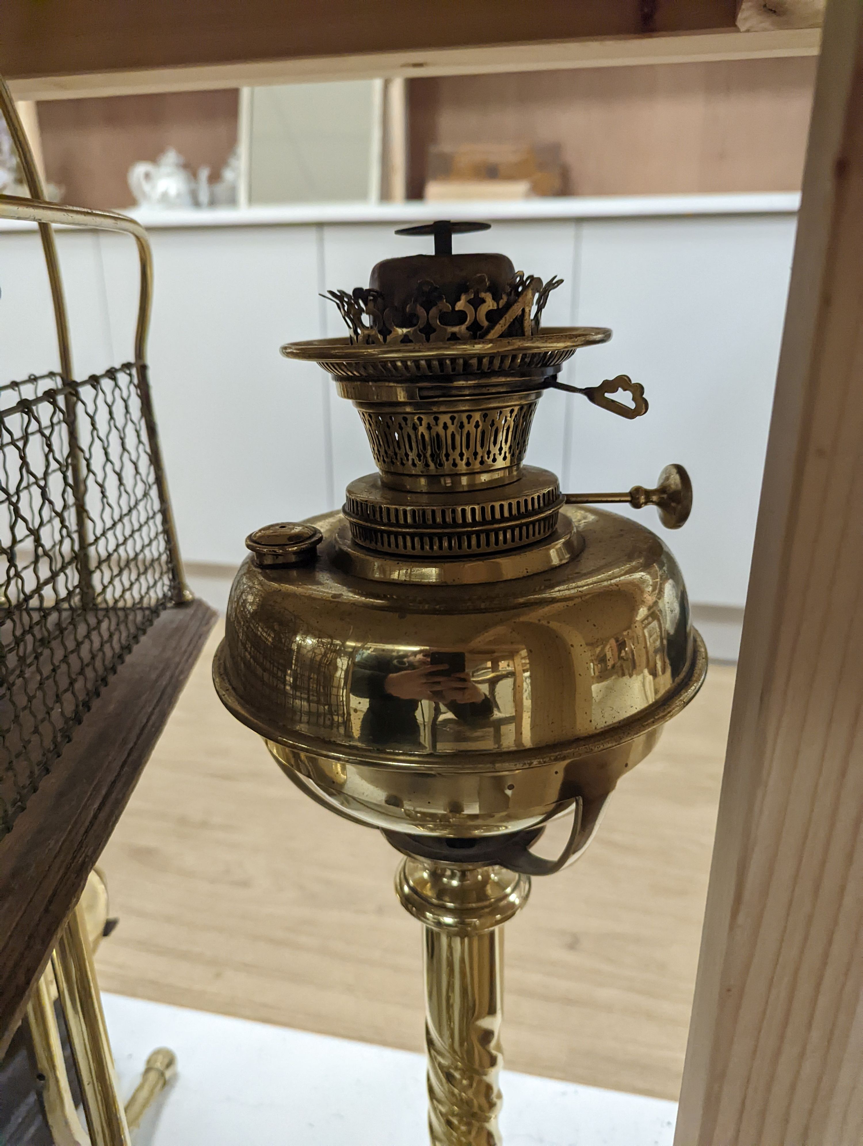 A brass magazine stand, a pair of scales, four candlesticks and a tall brass oil lamp base, Oil lamp 58 cms high.